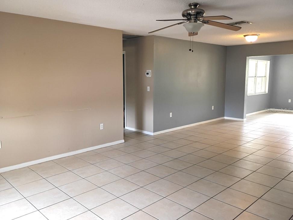 An open-concept living area features beige and gray walls, tile flooring, and a ceiling fan — 1208 S CANAL BOULEVARD, SEBRING, FL