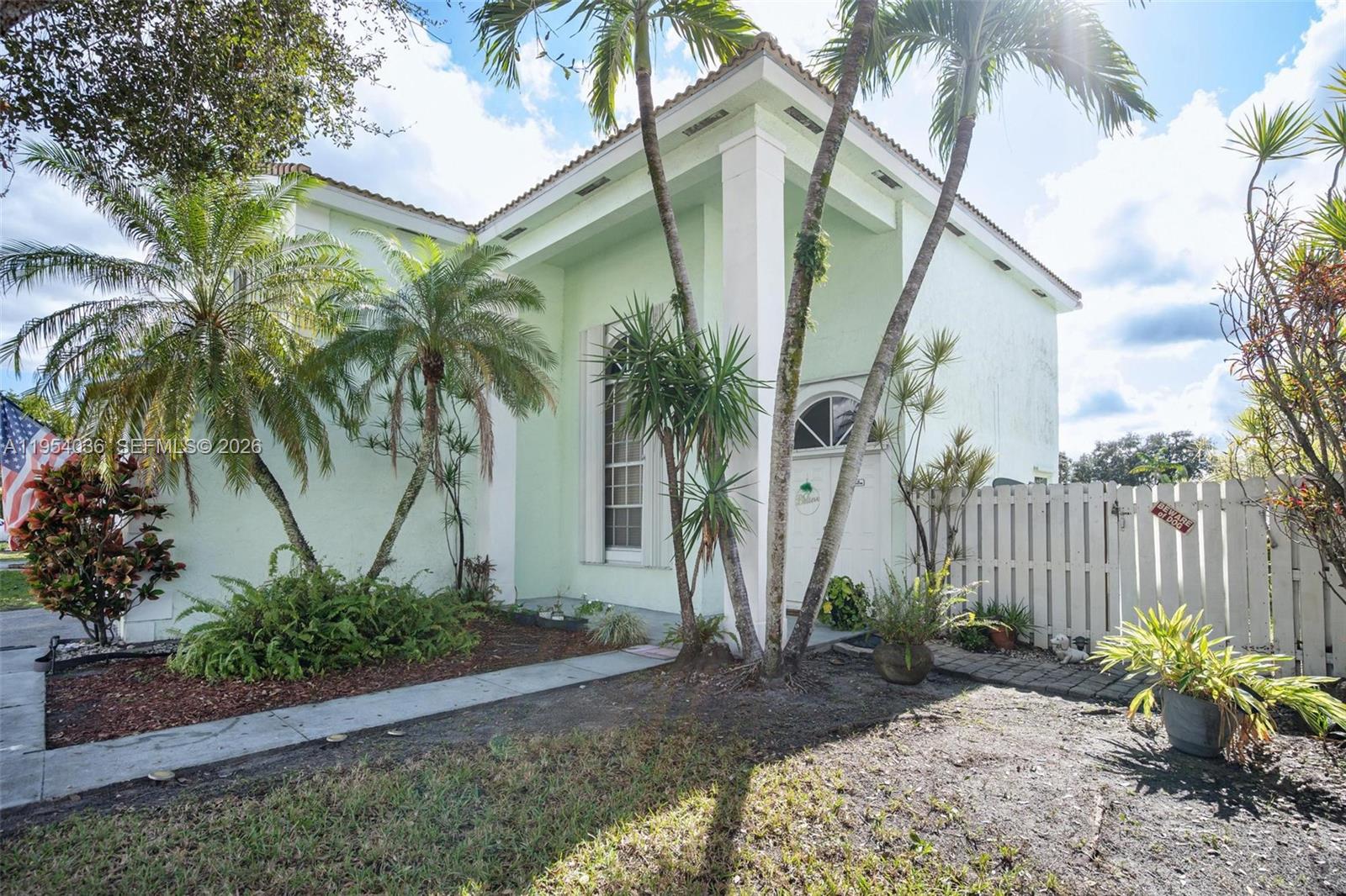 A light green house exterior features palm trees, a white fence, and a front entrance — 13930 Oak Ridge Dr, Davie FL 33325, DAVIE, FL