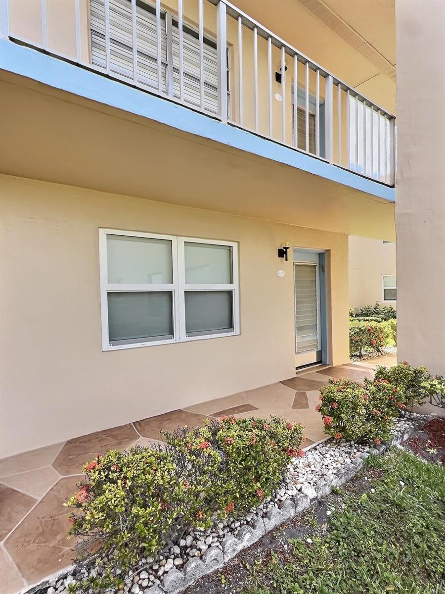 A ground-level apartment entrance features a tiled patio, a window, and a second-story balcony — 199 Burgundy E, Delray Beach FL 33484, DELRAY BEACH, FL