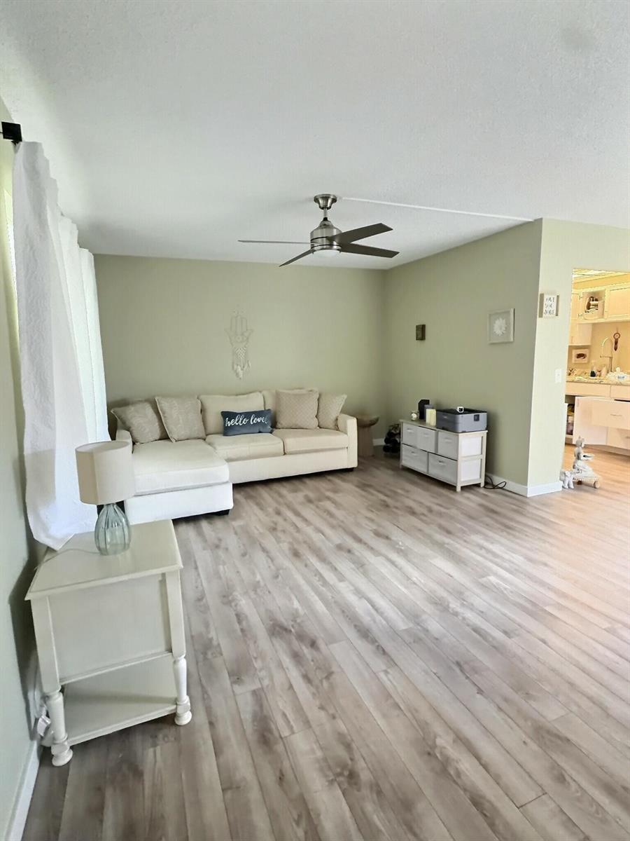 A living room features light green walls, wood-look flooring, a white sectional sofa, and a ceiling fan — 199 Burgundy E, Delray Beach FL 33484, DELRAY BEACH, FL