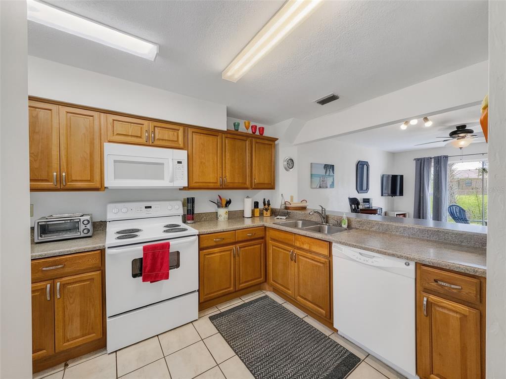 A kitchen features wood cabinets, white appliances, a double sink, and tile flooring — 175 YORKTOWNE DRIVE UNIT UT11, DAYTONA BEACH, FL