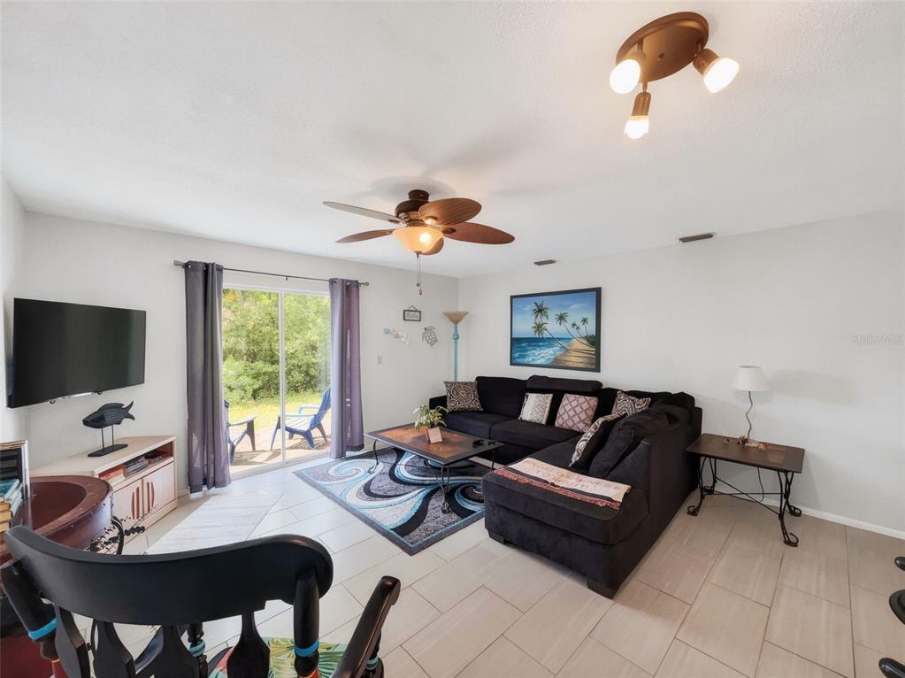 A living room features a black sectional sofa, a patterned area rug, and sliding glass doors — 175 YORKTOWNE DRIVE UNIT UT11, DAYTONA BEACH, FL