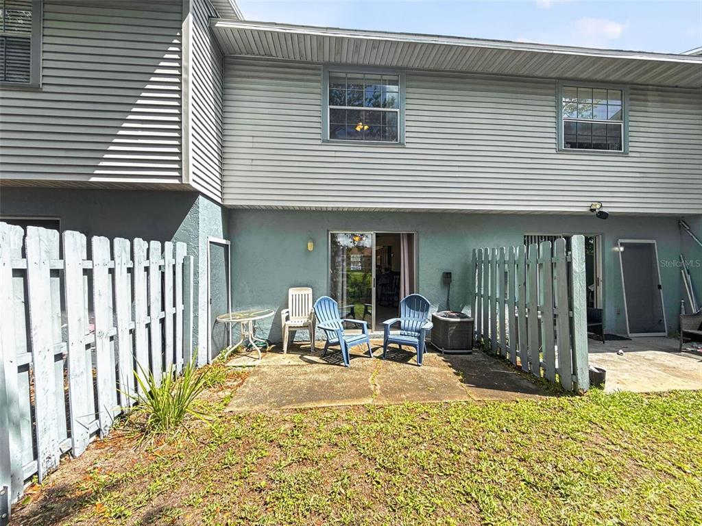 A backyard patio features a concrete slab, blue chairs, and a white wooden fence — 175 YORKTOWNE DRIVE UNIT UT11, DAYTONA BEACH, FL