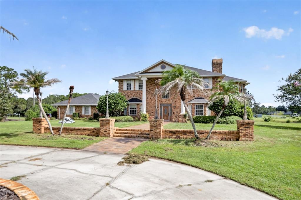 A two-story brick house with a columned entrance and a low brick perimeter wall — 4657 HICKORY TREE ROAD, ST CLOUD, FL