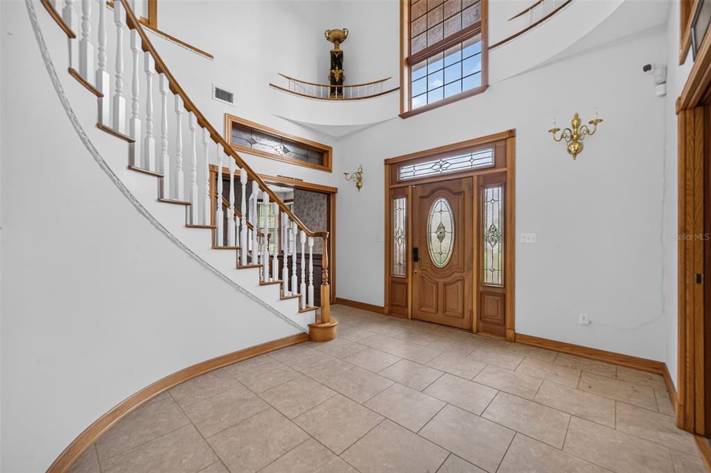 A bright foyer features a curved staircase, tile flooring, and a large wooden front door — 4657 HICKORY TREE ROAD, ST CLOUD, FL