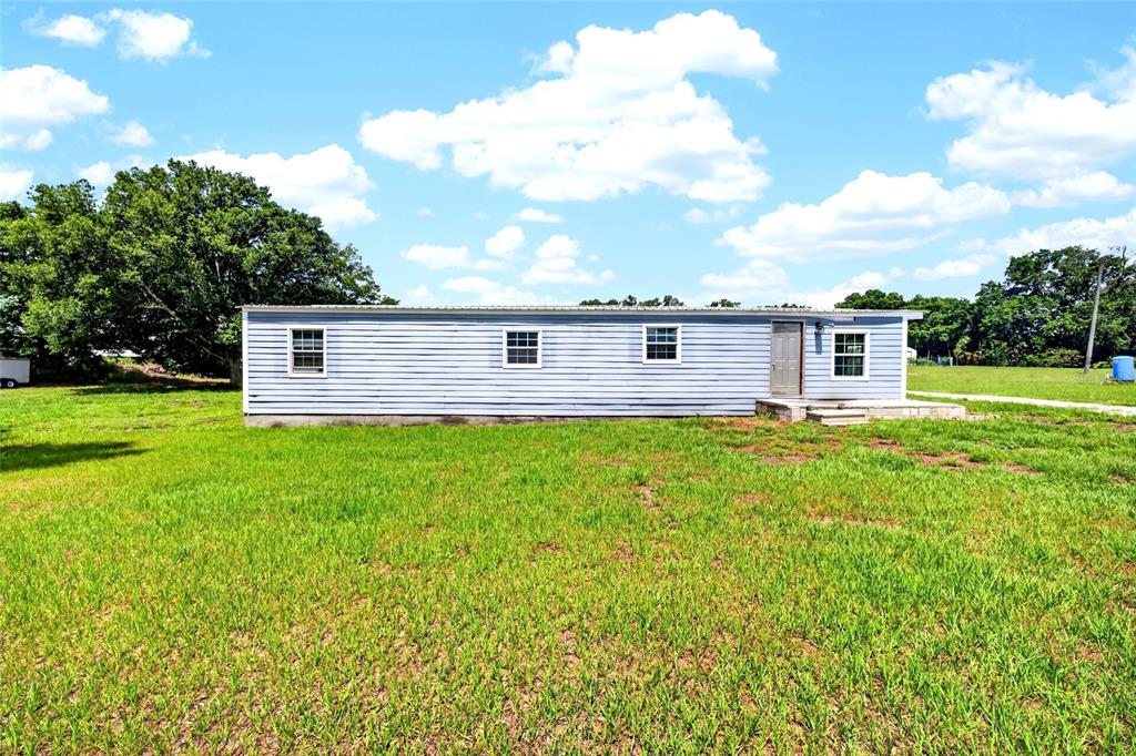 A light blue, single-story manufactured home sits in a large, grassy field under a cloudy sky — 4162 LAUGHLIN ROAD, MOUNT DORA, FL
