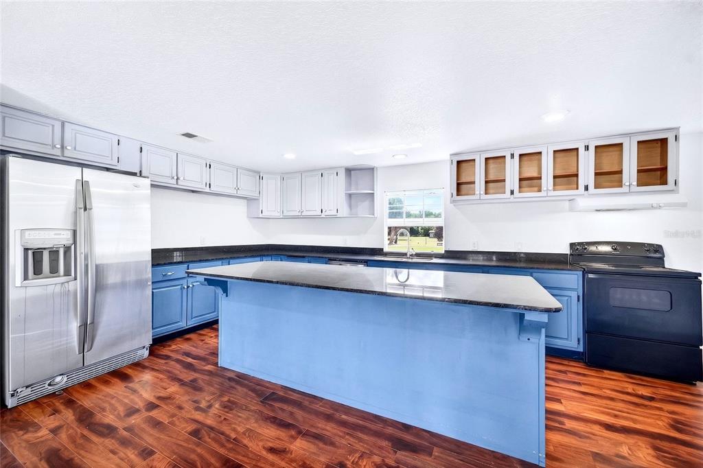 A kitchen features blue lower cabinets, light gray upper cabinets, black countertops, and wood flooring — 4162 LAUGHLIN ROAD, MOUNT DORA, FL
