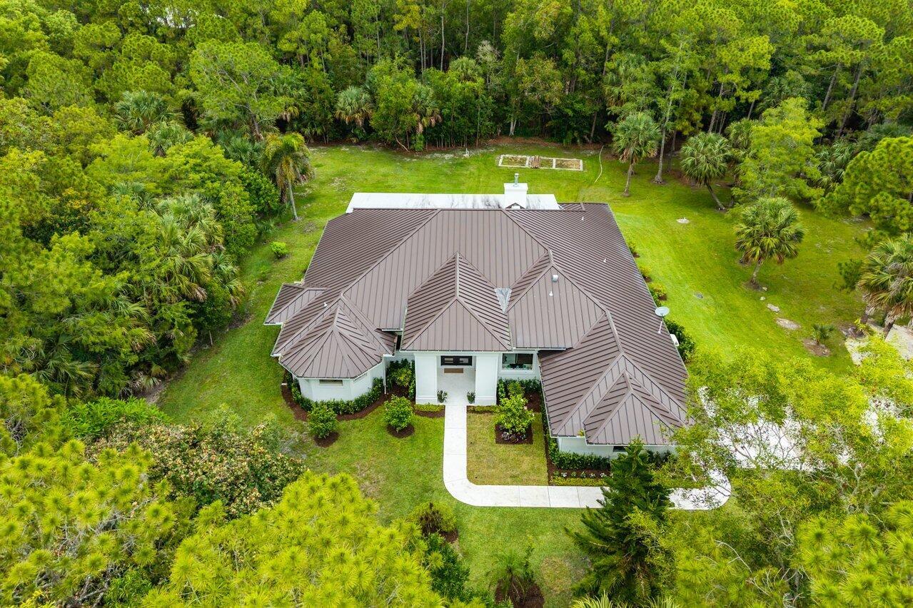 An aerial view shows a house with a dark metal roof surrounded by lush trees — 11871 Randolph Siding Road N, Jupiter FL 33478, JUPITER, FL
