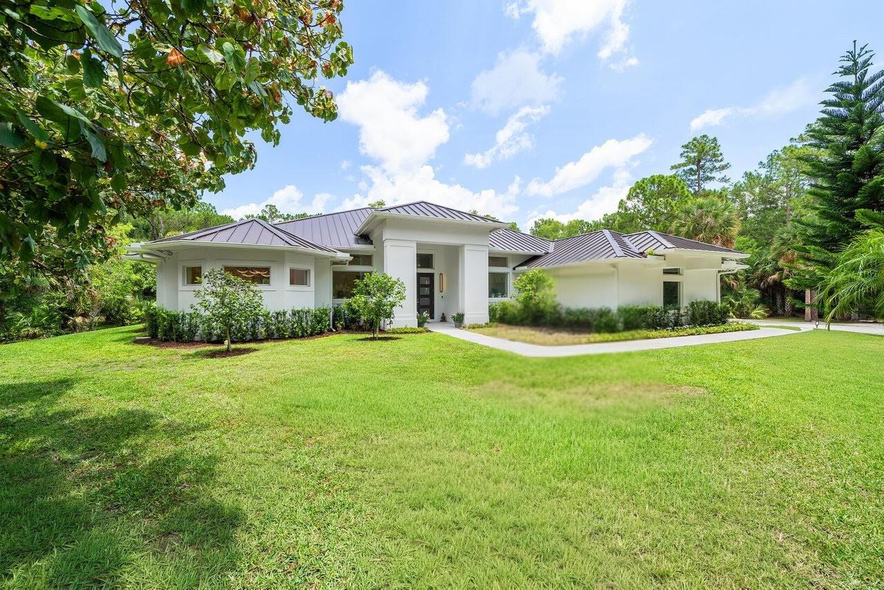A single-story white house with a dark metal roof sits on a grassy lawn — 11871 Randolph Siding Road N, Jupiter FL 33478, JUPITER, FL
