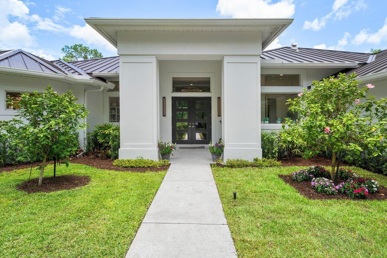 A concrete walkway leads to the front entrance of a white house with a metal roof — 11871 Randolph Siding Road N, Jupiter FL 33478, JUPITER, FL