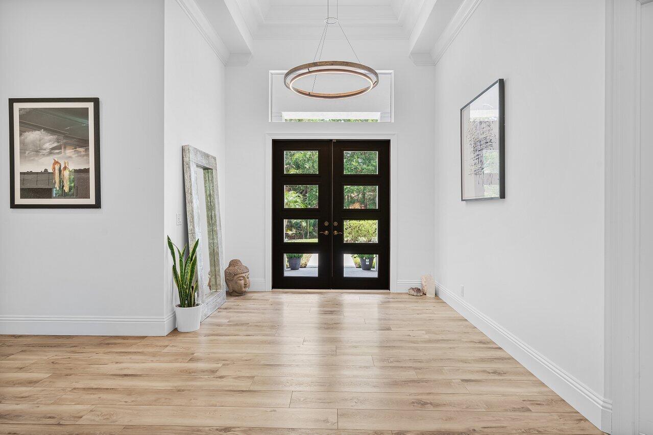 A bright entryway features light wood flooring, white walls, and a black double front door — 11871 Randolph Siding Road N, Jupiter FL 33478, JUPITER, FL