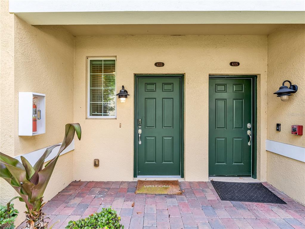 A paved entryway features two green doors with house numbers and a wall-mounted fire extinguisher — 4213 EXPEDITION WAY UNIT 107, OSPREY, FL