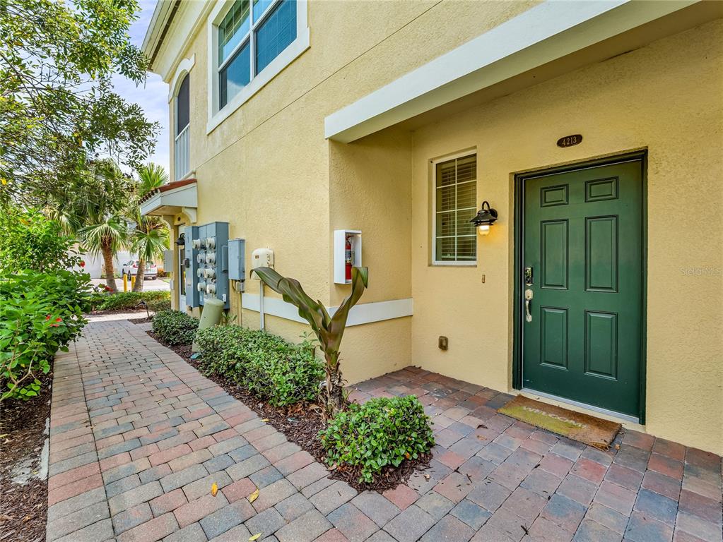 A paved walkway leads to the green front door of a yellow stucco building — 4213 EXPEDITION WAY UNIT 107, OSPREY, FL