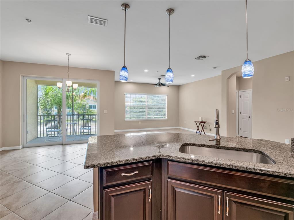 A kitchen island with a granite countertop and sink overlooks an open living area — 4213 EXPEDITION WAY UNIT 107, OSPREY, FL