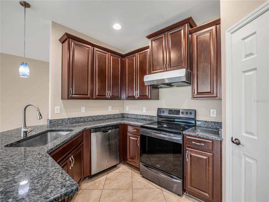 A kitchen features dark wood cabinets, granite countertops, stainless steel appliances, and tile flooring — 4213 EXPEDITION WAY UNIT 107, OSPREY, FL