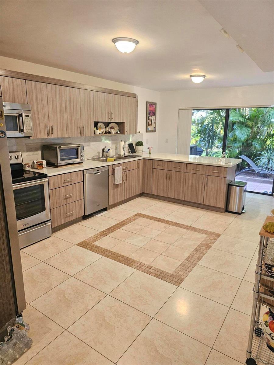 A kitchen features light wood cabinets, stainless steel appliances, and a tiled floor with inlay — 1412 SW 110th Way, Davie FL 33324, DAVIE, FL