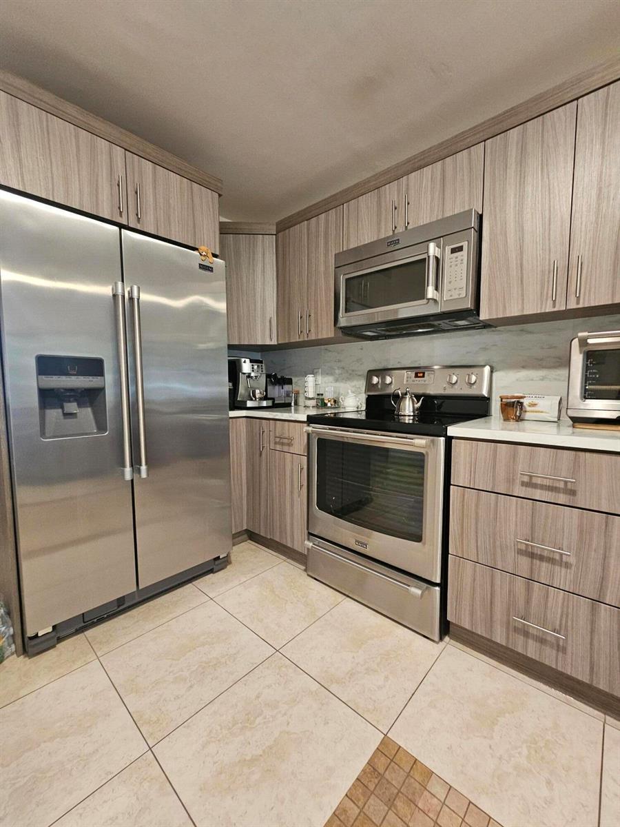 A kitchen features stainless steel appliances, wood-grain cabinets, and light-colored tile flooring — 1412 SW 110th Way, Davie FL 33324, DAVIE, FL