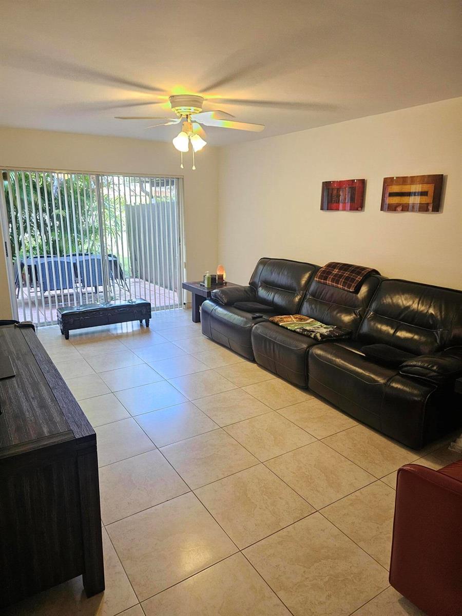 A living room features beige tile flooring, a black leather sofa, and a sliding glass door — 1412 SW 110th Way, Davie FL 33324, DAVIE, FL