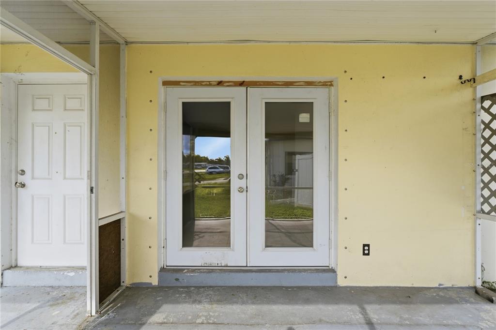 A covered porch features a yellow wall, a white single door, and white French doors — 21123 GLENDALE AVENUE, PORT CHARLOTTE, FL