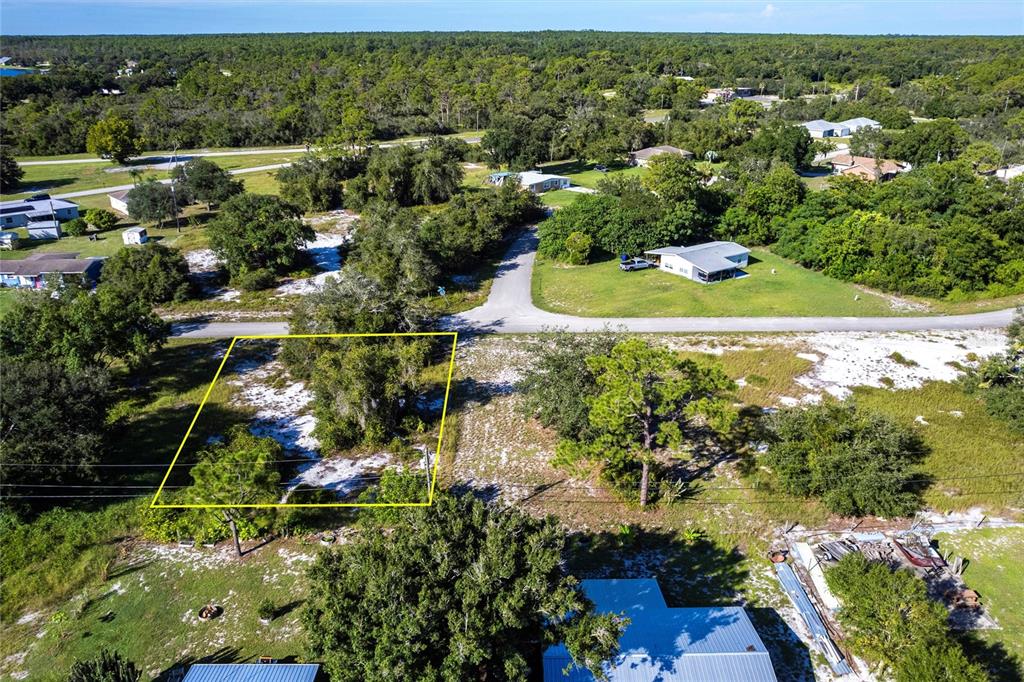 An aerial view shows a vacant, tree-covered lot outlined in yellow near a paved road — 913 HOLLYHOCK COURT, LAKE PLACID, FL