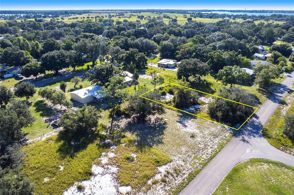 An aerial view shows a vacant, tree-covered lot outlined in yellow next to a paved road — 913 HOLLYHOCK COURT, LAKE PLACID, FL