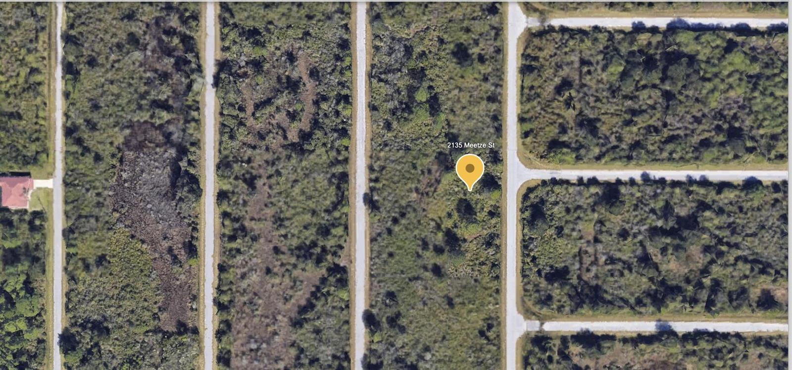 This aerial view shows a vacant, wooded residential lot situated between two paved roads — 2135 Meetze Street, FL 33953, FL