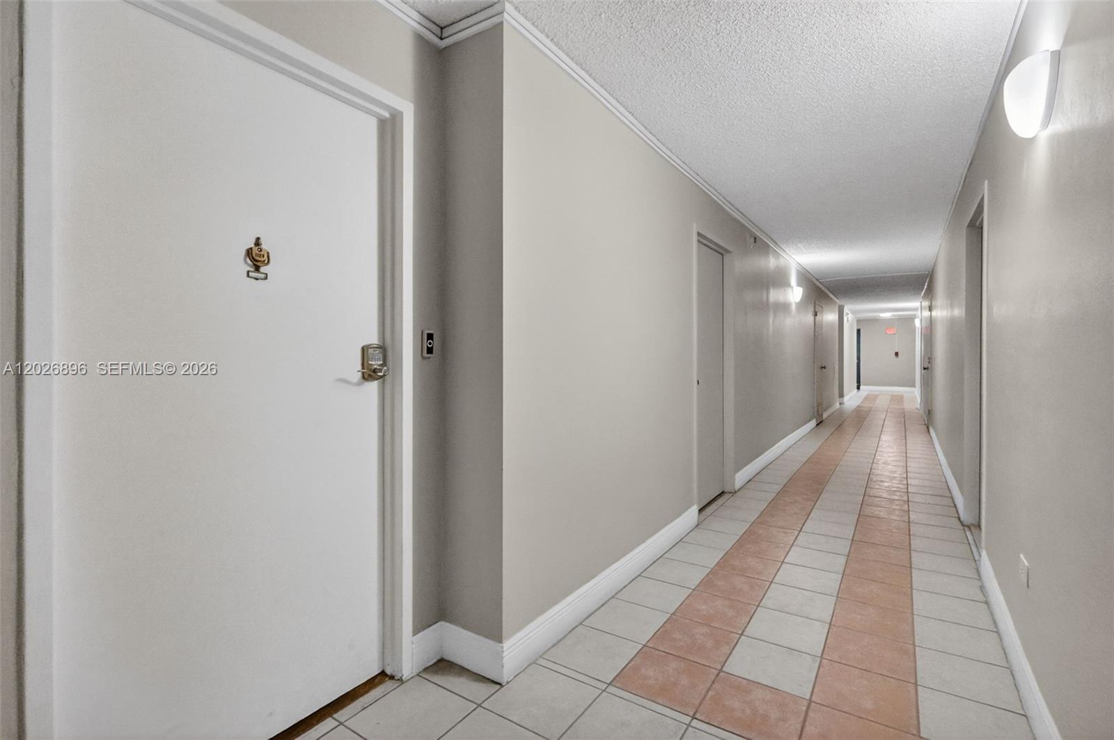 A long, narrow apartment hallway features beige walls, tiled flooring, and several closed doors — 7135 Collins Ave # 1124, Miami Beach FL 33141, MIAMI BEACH, FL