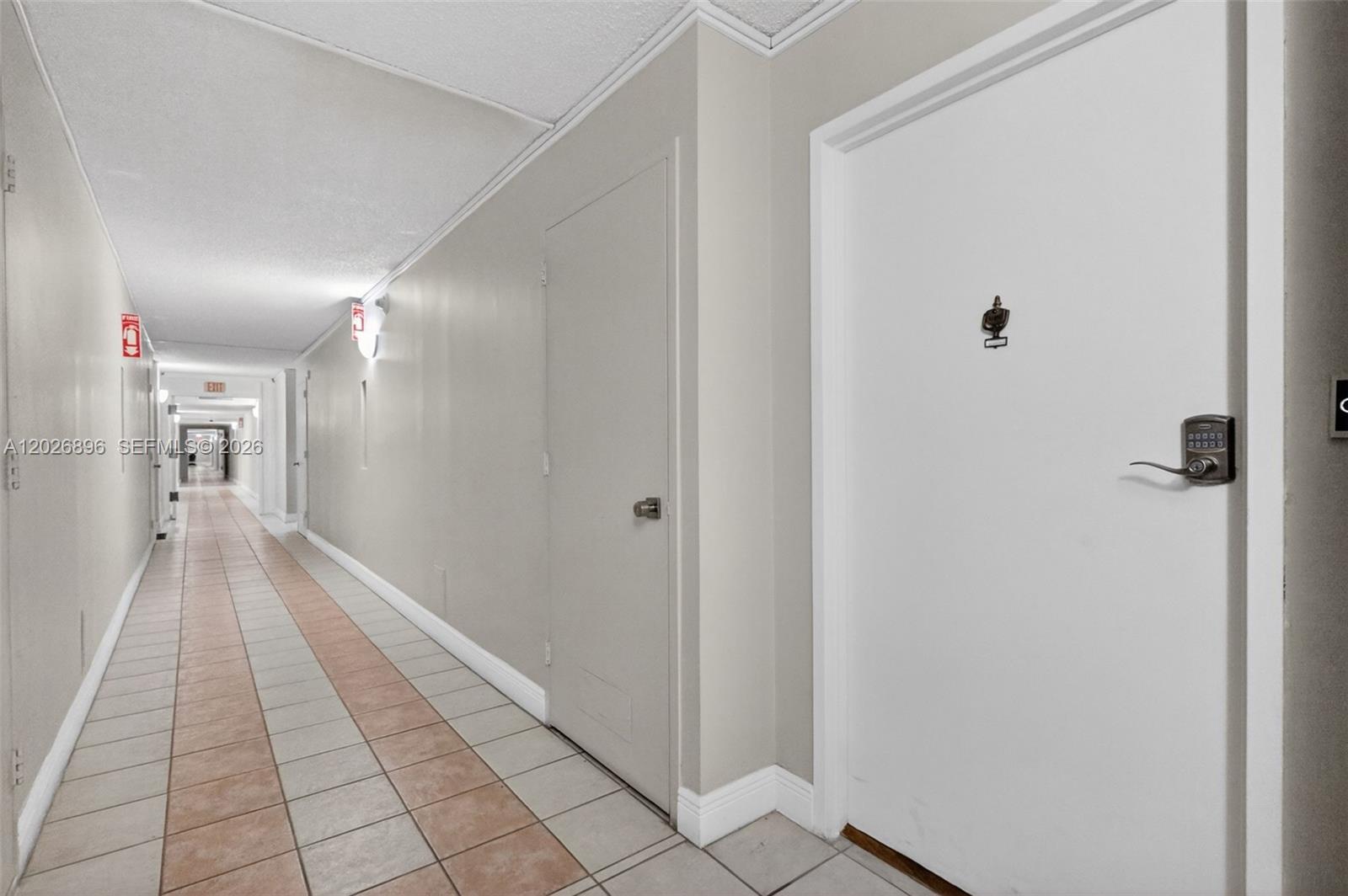 A long apartment building hallway with tiled floors, beige walls, and white doors — 7135 Collins Ave # 1124, Miami Beach FL 33141, MIAMI BEACH, FL