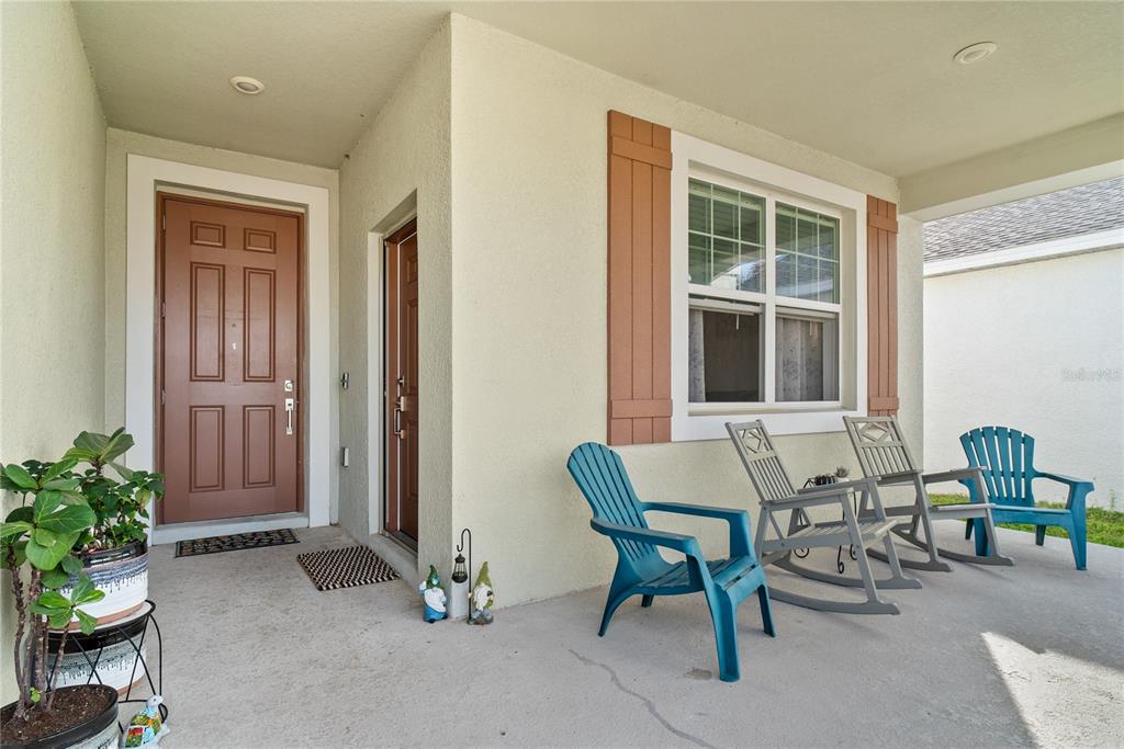 A covered front porch features a brown door, a window with shutters, and four chairs — 1778 GOOD NEIGHBOR LOOP, KISSIMMEE, FL