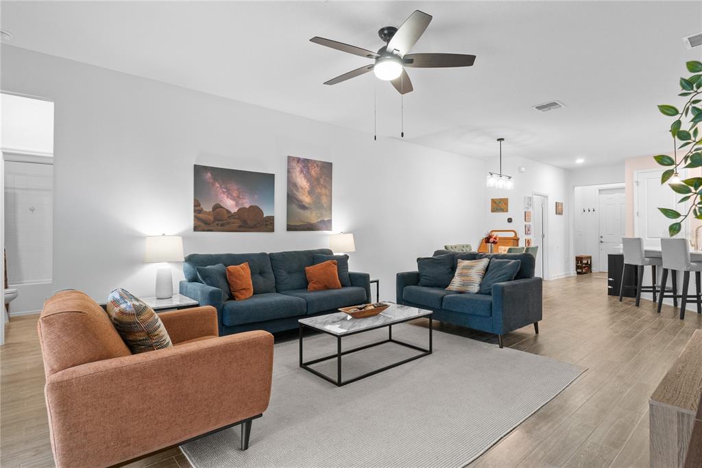 A living room features blue sofas, an orange armchair, a coffee table, and a ceiling fan — 1778 GOOD NEIGHBOR LOOP, KISSIMMEE, FL