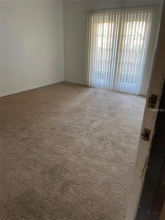 An empty room with beige carpeting and vertical blinds covering a sliding glass door — 315 WYMORE ROAD UNIT 104, ALTAMONTE SPRINGS, FL