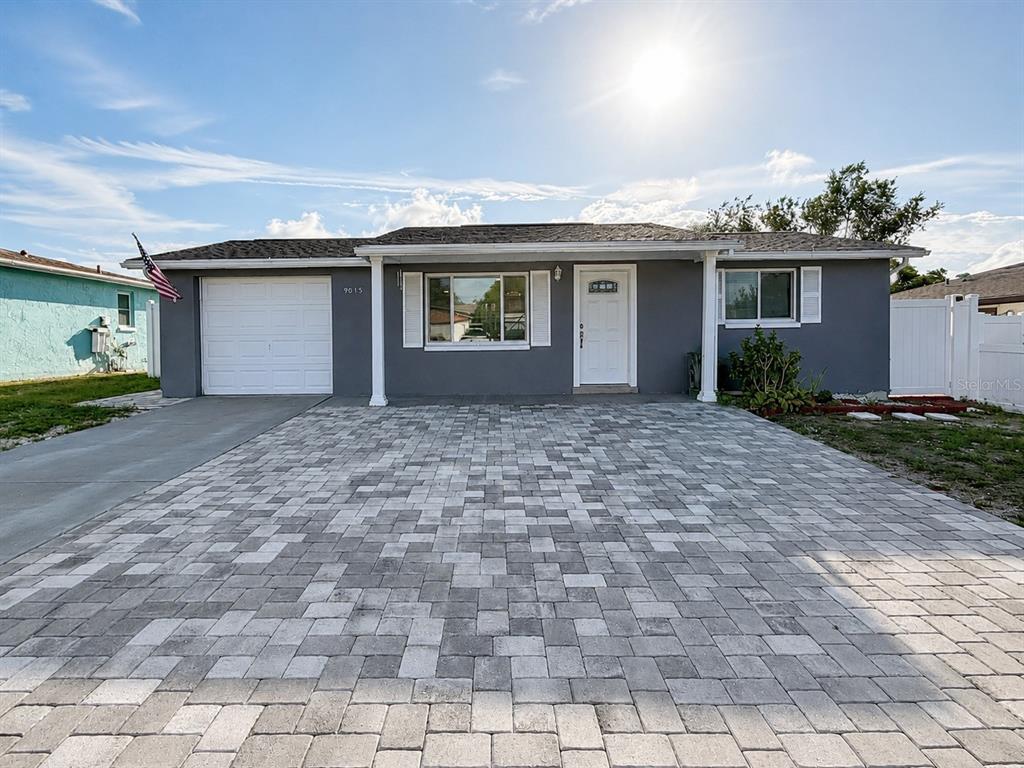 A gray single-story house features a white garage door, a paved driveway, and white shutters — 9015 PROSPERITY LANE, PORT RICHEY, FL