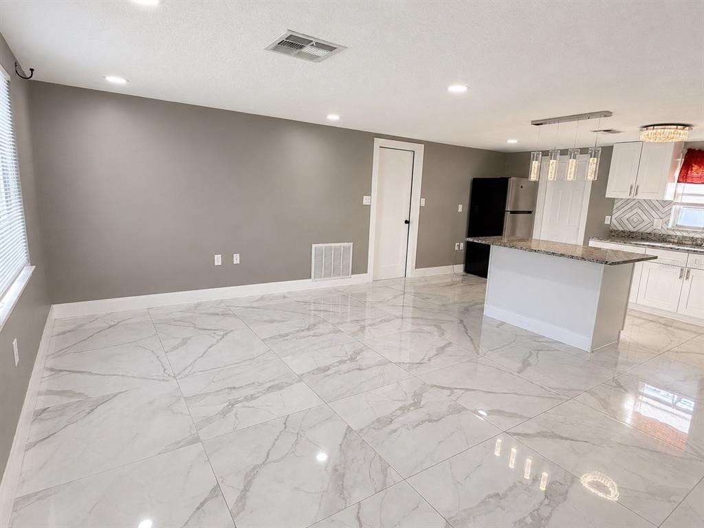 A bright, open-concept room features large white marble-look floor tiles and a kitchen island — 9015 PROSPERITY LANE, PORT RICHEY, FL