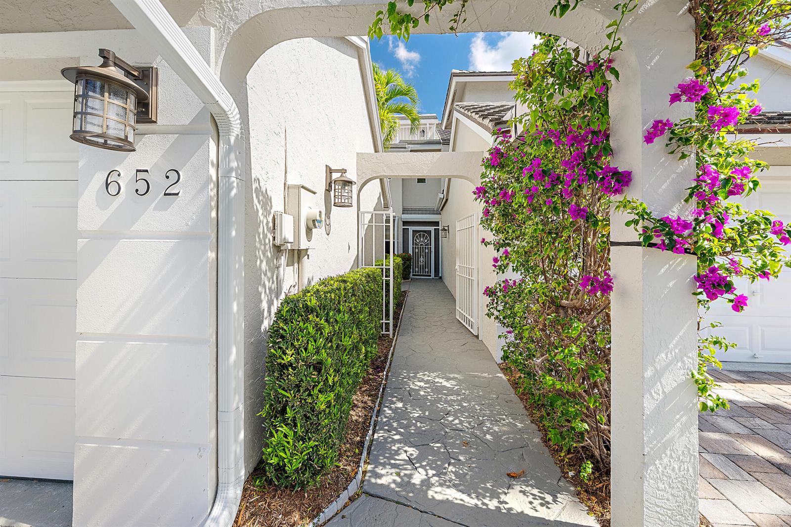 A stone walkway leads through a white archway toward a front door with purple bougainvillea — 1000 N Us Highway 1 # 652, Jupiter FL 33477, JUPITER, FL