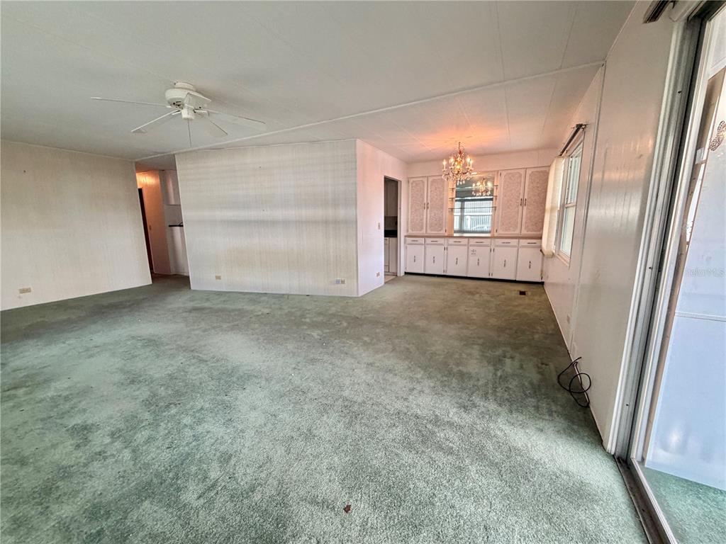 A living and dining area with green carpeting, white paneled walls, and built-in cabinetry — 132 TAMARISK WAY, LEESBURG, FL