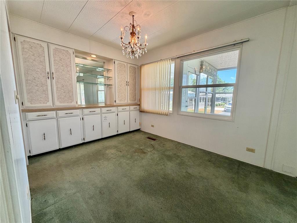 A dining room features green carpeting, white cabinetry with a mirrored hutch, and a chandelier — 132 TAMARISK WAY, LEESBURG, FL