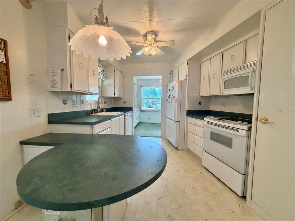 A kitchen features white cabinets, dark green countertops, white appliances, and a breakfast bar — 132 TAMARISK WAY, LEESBURG, FL