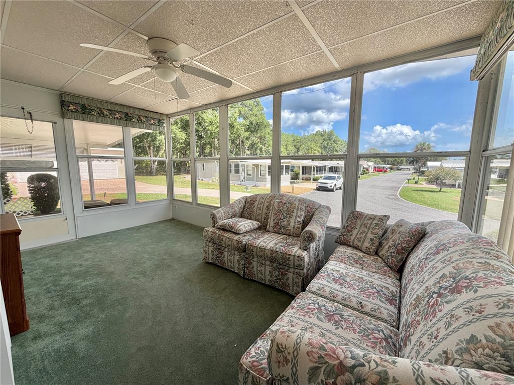 A sunroom features green carpeting, a ceiling fan, and floral furniture overlooking a residential street — 132 TAMARISK WAY, LEESBURG, FL