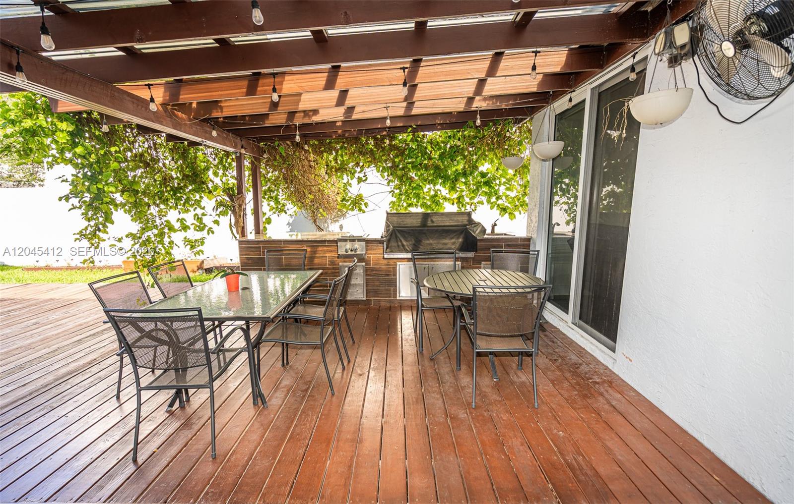 A wooden deck features a pergola, outdoor dining sets, and a built-in grill station — PEMBROKE PINES, FL