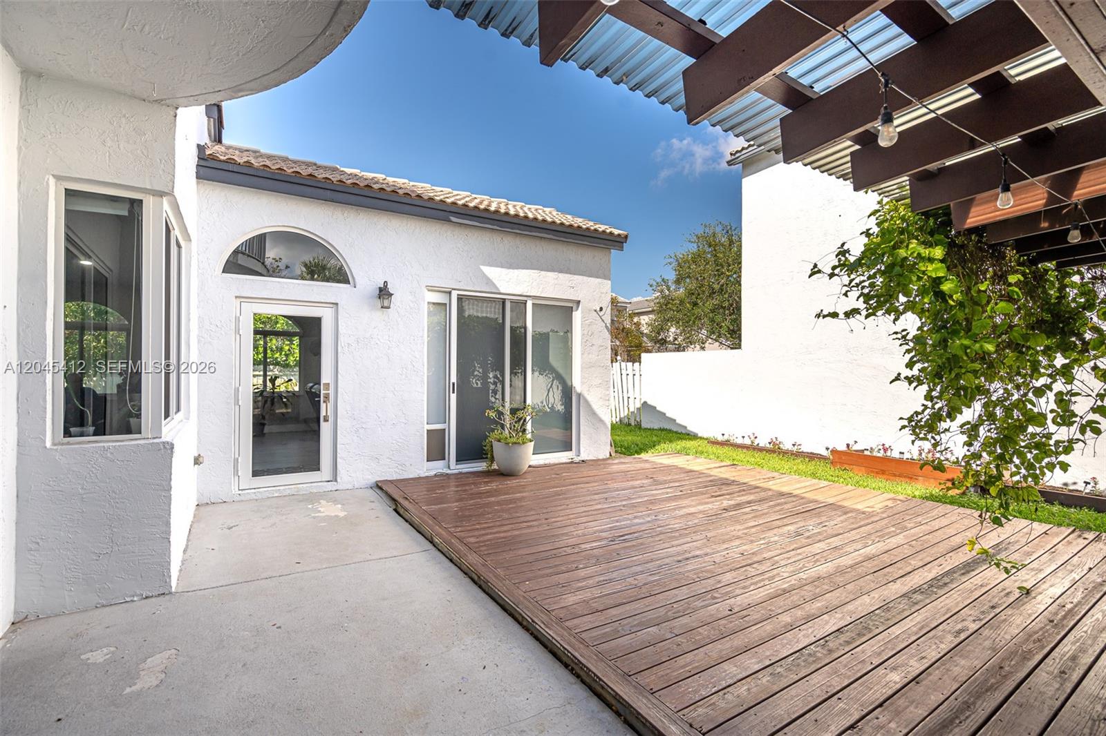 A backyard patio features a wooden deck, a concrete area, and a pergola with string lights — PEMBROKE PINES, FL
