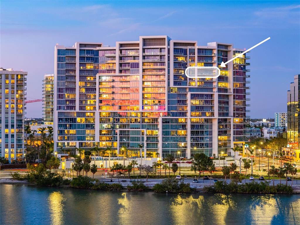 An exterior view of a modern high-rise apartment building at dusk with a highlighted balcony — 1155 N GULFSTREAM AVENUE UNIT 1607, SARASOTA, FL