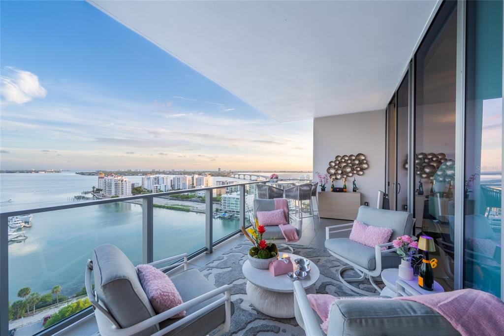 A furnished balcony overlooks a bay with a bridge and city skyline in the distance — 1155 N GULFSTREAM AVENUE UNIT 1607, SARASOTA, FL