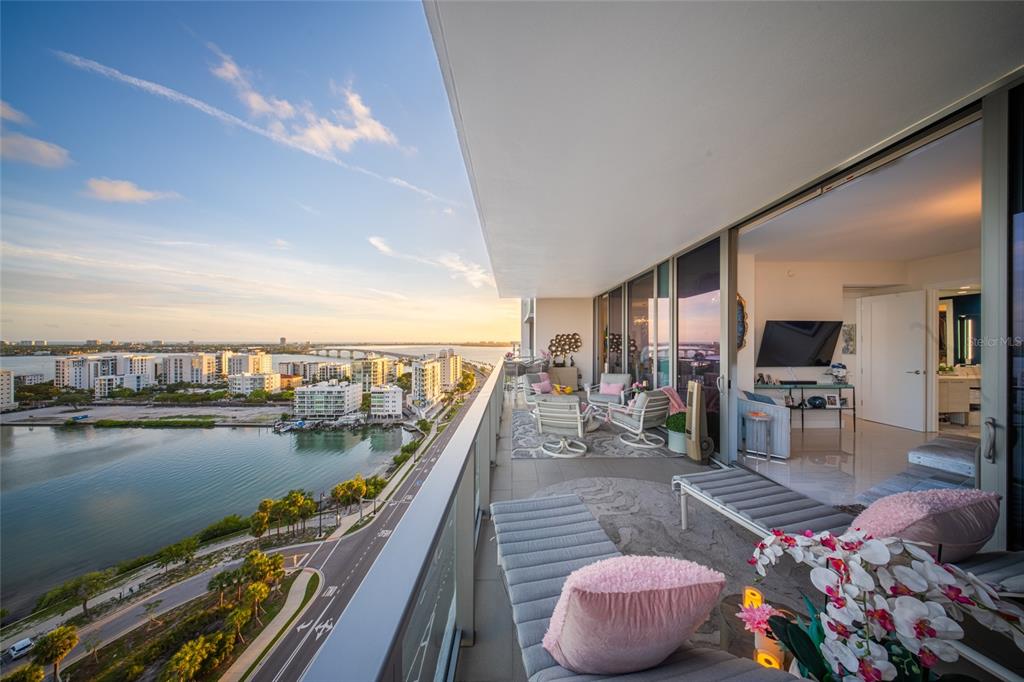 A high-rise balcony features outdoor seating overlooking a coastal city, water, and a bridge — 1155 N GULFSTREAM AVENUE UNIT 1607, SARASOTA, FL