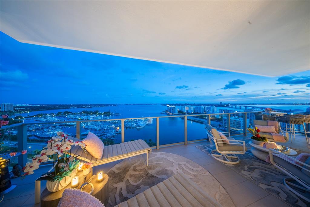 A high-rise balcony features lounge chairs, outdoor furniture, and a panoramic view of a marina — 1155 N GULFSTREAM AVENUE UNIT 1607, SARASOTA, FL