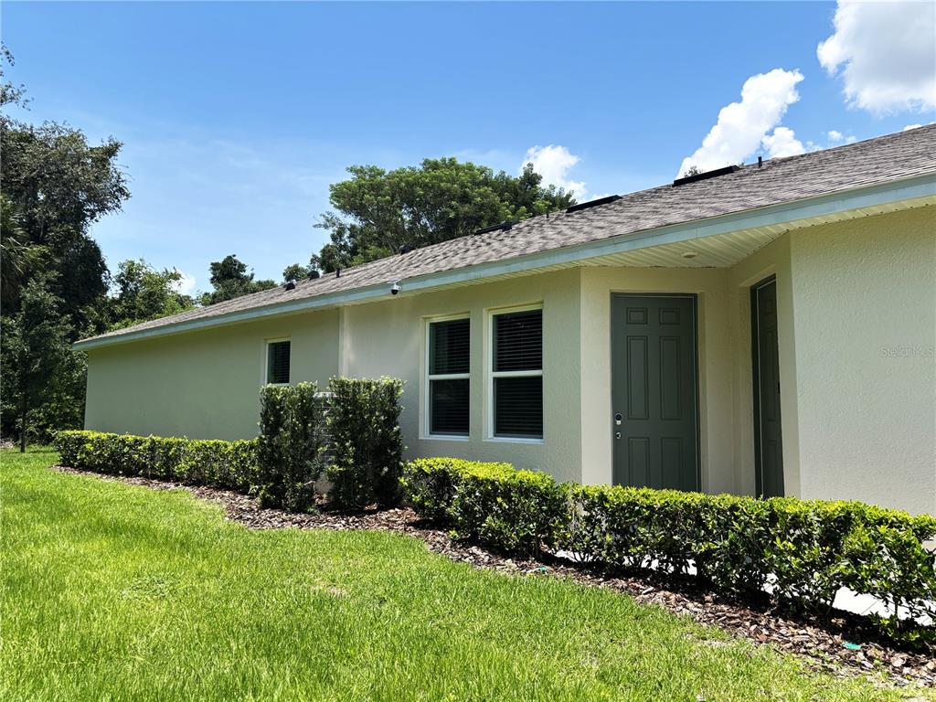 A side view of a light-colored house exterior with a green door and landscaping — 2168 GREENWOOD OAK DRIVE, OCOEE, FL