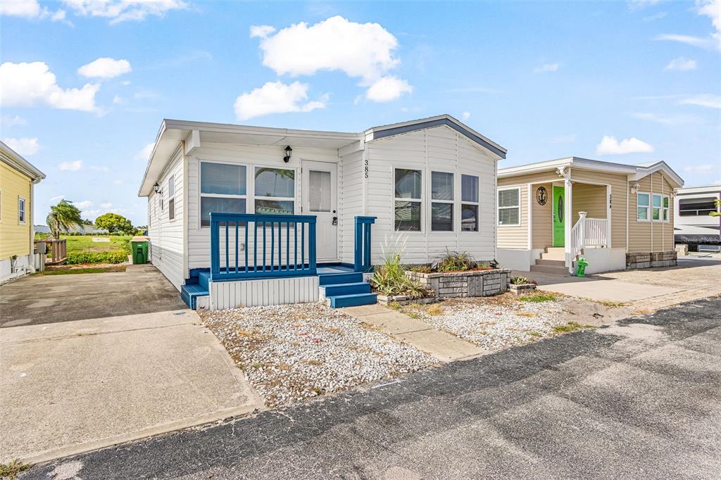 A white manufactured home with a blue porch and gravel front yard under a blue sky — 1475 FLAMINGO DRIVE UNIT 385, ENGLEWOOD, FL