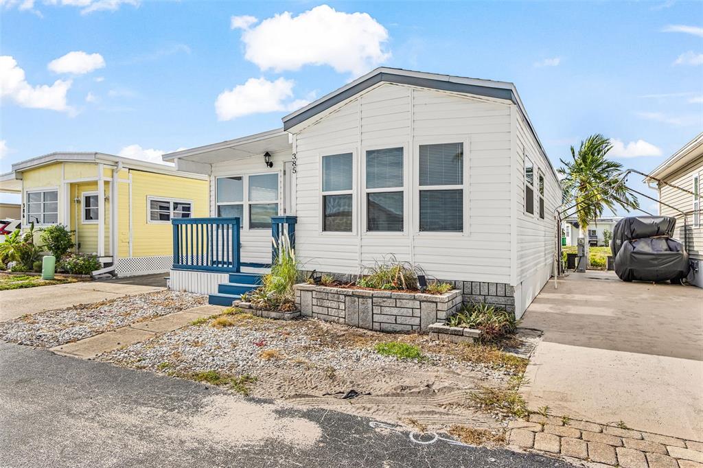 A white manufactured home with a blue porch and a stone planter in the front yard — 1475 FLAMINGO DRIVE UNIT 385, ENGLEWOOD, FL