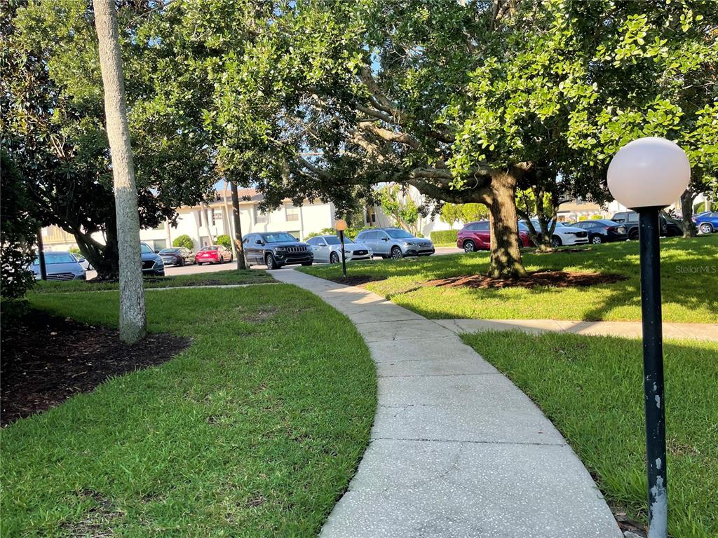 A concrete walkway winds through a grassy area with mature trees and parked cars — 200 MAITLAND AVENUE UNIT 182, ALTAMONTE SPRINGS, FL
