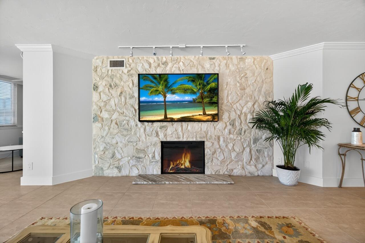 A living room features a stone fireplace wall with a mounted television and tile flooring — 5790 Jimmy Buffett Mem Highway, Vero Beach FL 32963, VERO BEACH, FL