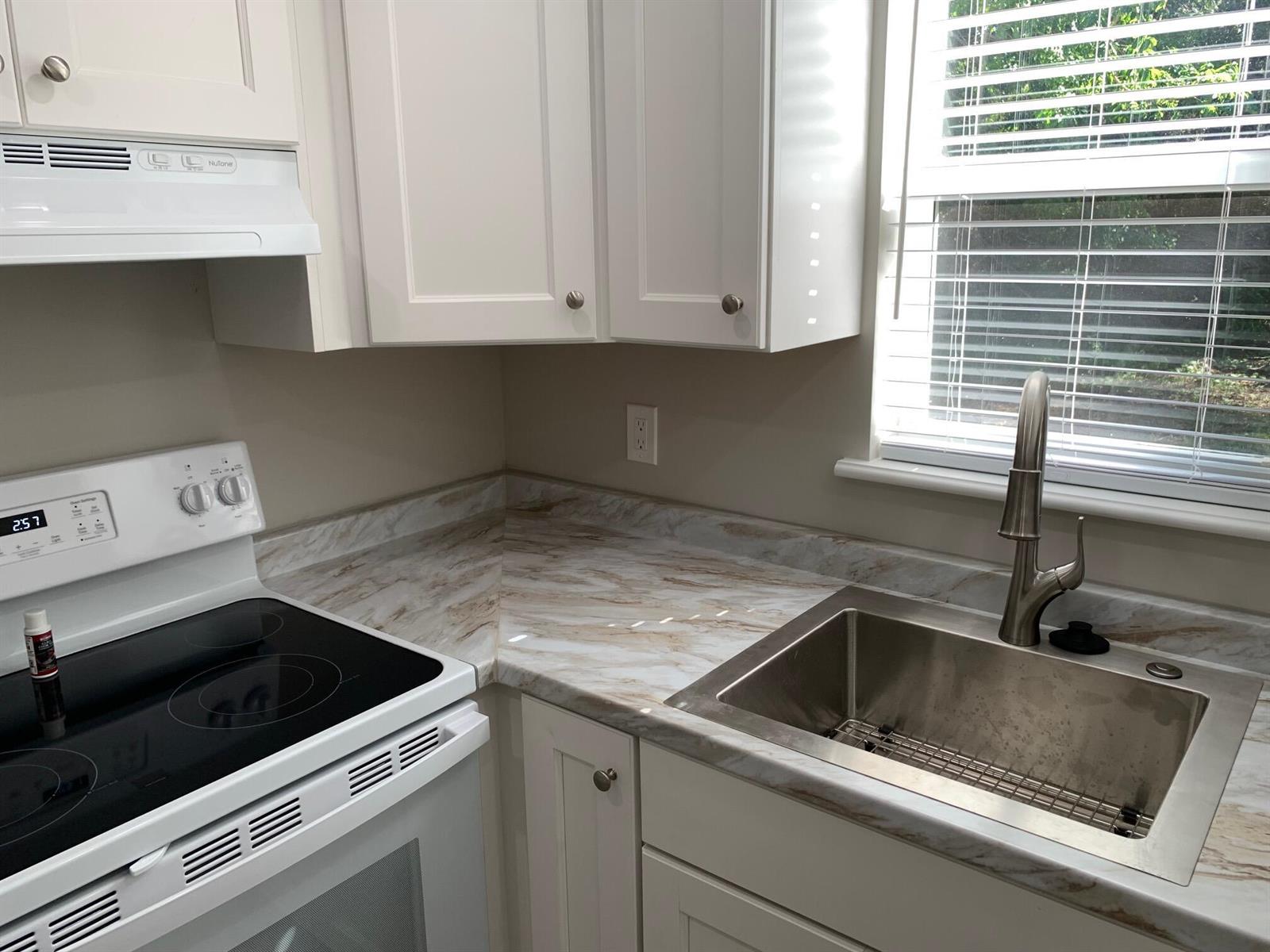 A kitchen features white cabinets, a marble-patterned laminate countertop, a stainless steel sink, and stove — 4220 NE Indian River Drive NE Unit 5, Jensen Beach FL 34957, JENSEN BEACH, FL
